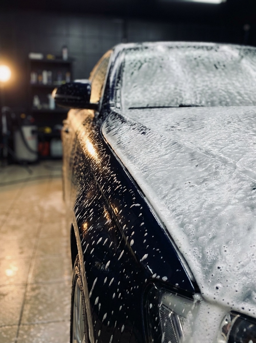 Snow foam over a dark car in the detailing bay